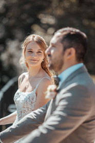 Hochzeit Erika und Demetris - Die Braut in einem weissen Hochzeitskleid schaut verliebt zum Bräutigam, welcher in einem grauen Anzug im Vordergrund steht.