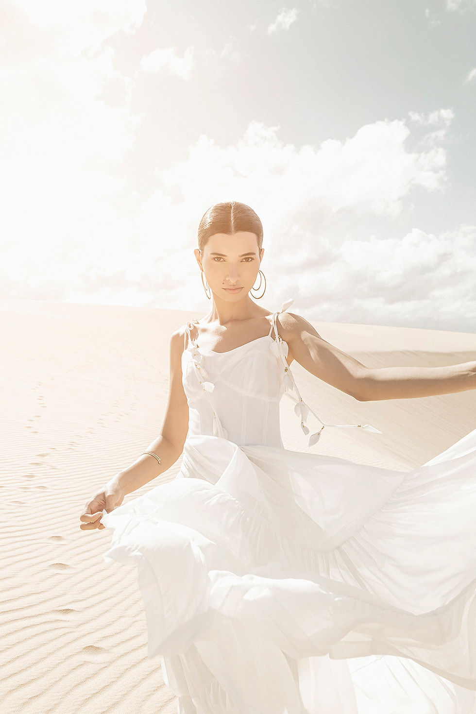 Modelo com vestido branco com a Duna de Jericoacoara ao fundo, luz estourada