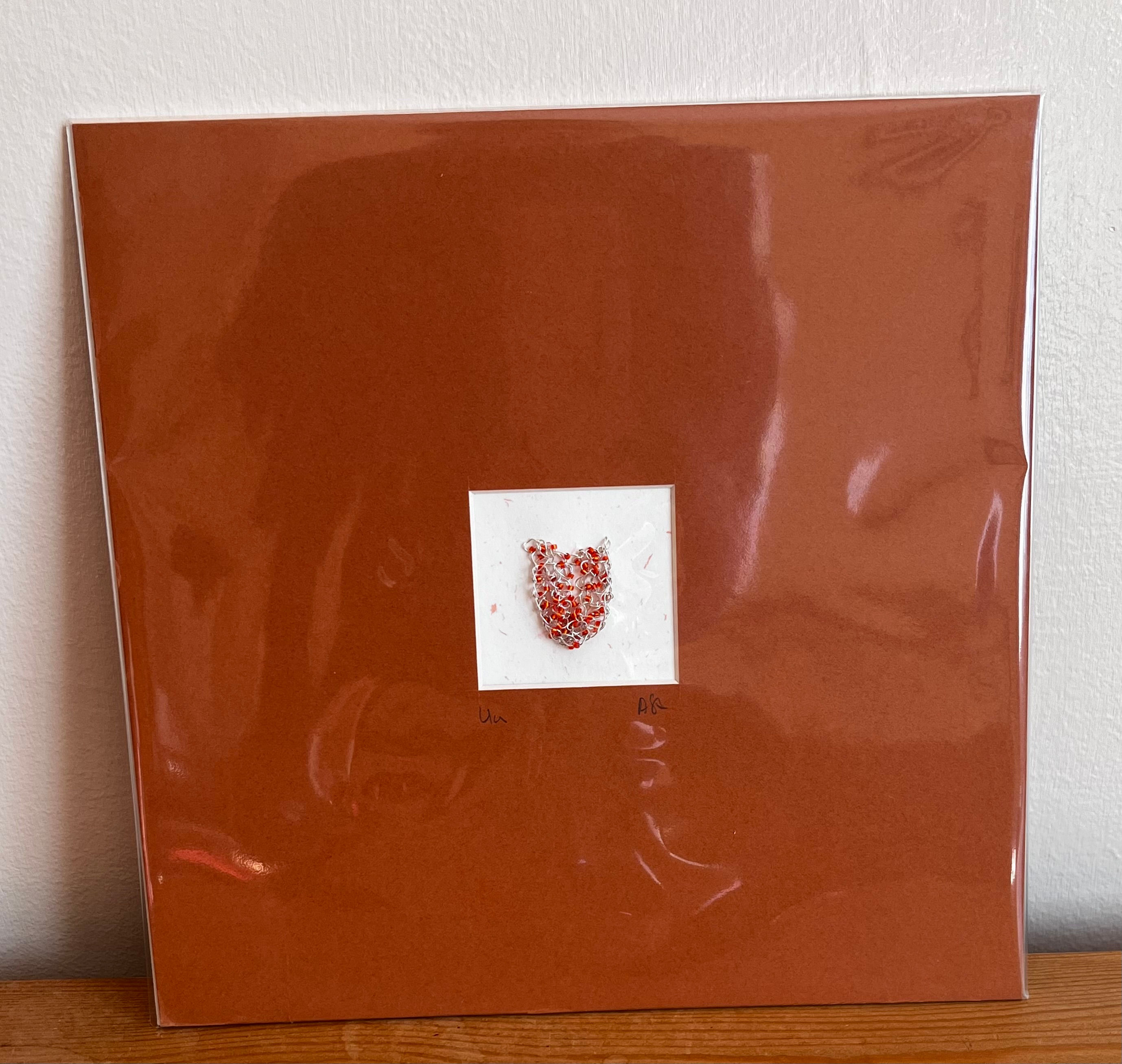 Mounted sample piece of knitted wire and orange glass beads