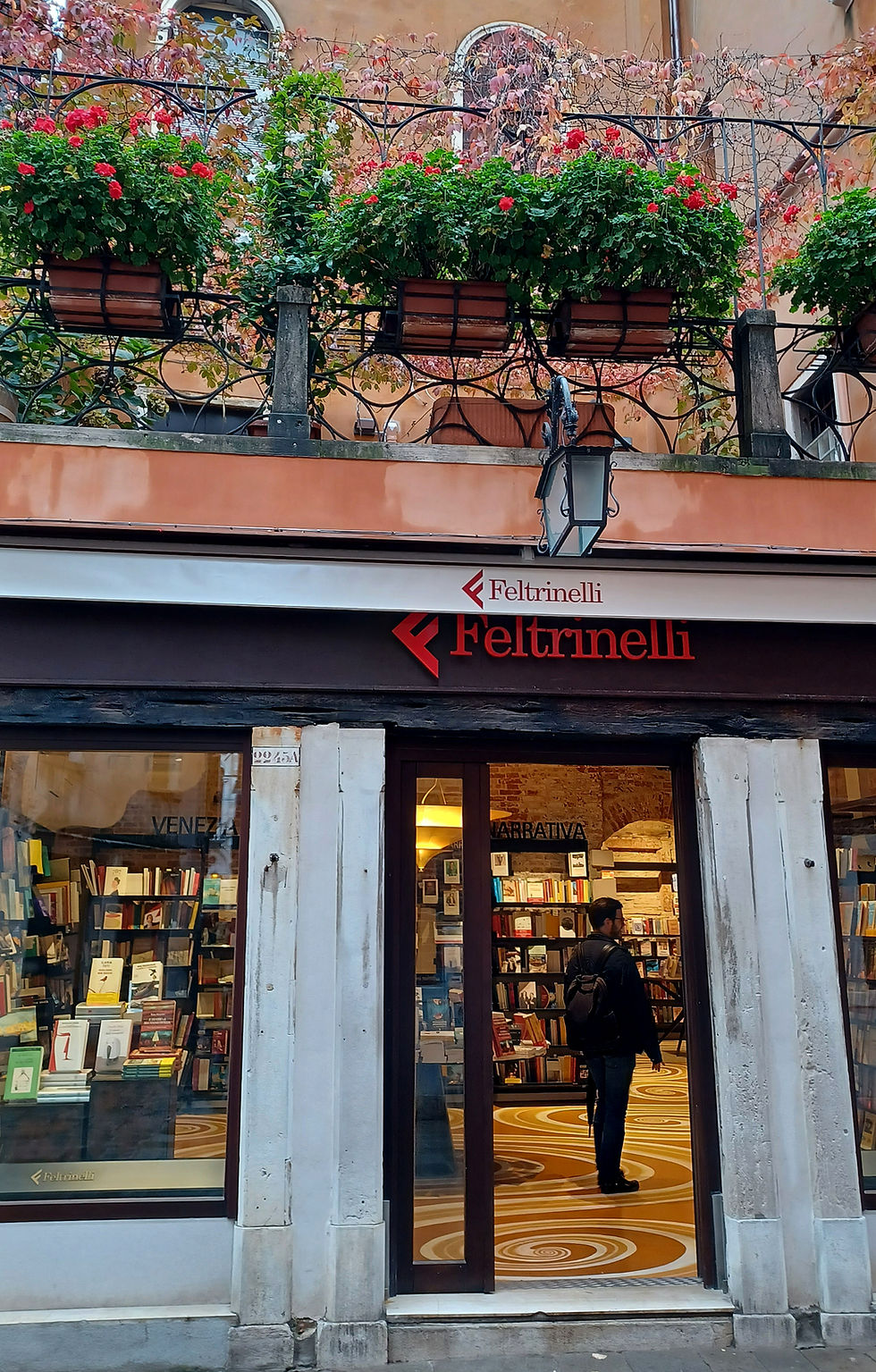 Bookshop in Venice with flowers on a balcony above the door
