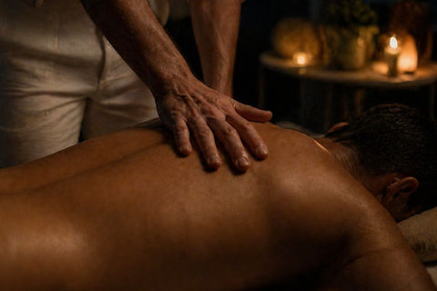 Hands resting on a man’s back during a quiet, candlelit massage, warm lighting and intimate stillness