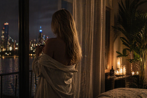 Woman standing by a window at night overlooking the Chicago skyline with candlelight in a softly lit room, intimate cinematic atmosphere