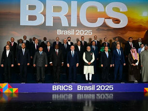 Group photo of BRICS Brasil 2025 summit participants standing on a stage beneath large “BRICS Brasil 2025” signage, with national leaders and delegates arranged in rows against a scenic backdrop.