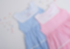 Two children’s tiered dresses in light blue and pink stripes, featuring white Peter Pan collars with embroidered birthday cak