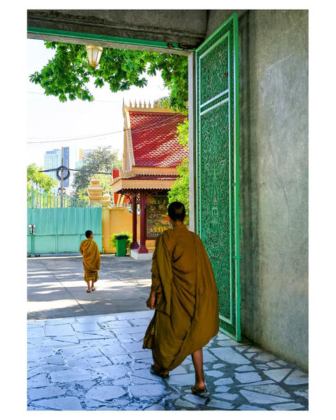 Two monks in saffron robes walk through large green temple gateway.