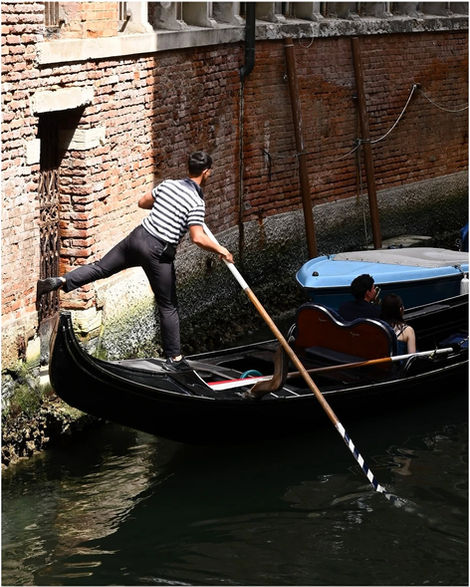 Gondolier propelling a black gondola with a long pole through a canal.