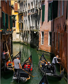 Three gondolas with people navigate a narrow canal in historic Venice.