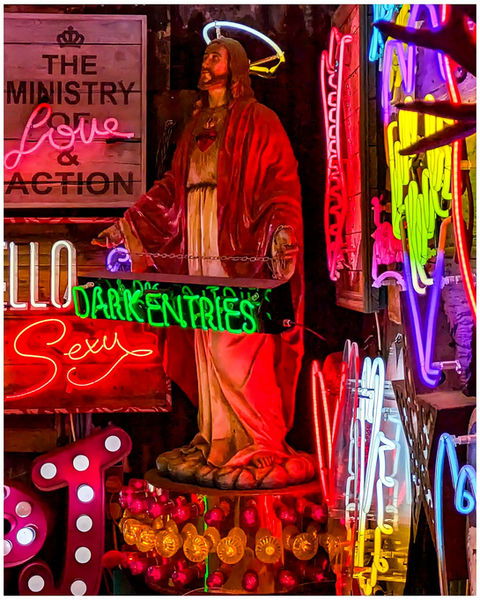 Jesus statue, neon halo, "LOVE & ACTION", "HELLO SEXY", "DARK ENTRIES", colorful signs.
