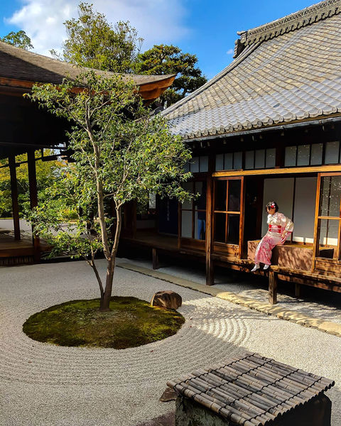 Woman in pink kimono seated at window overlooking serene Japanese garden.
