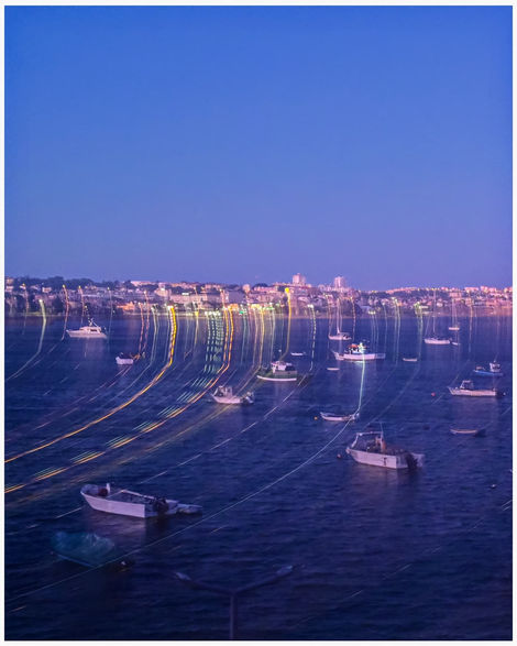 Dusk scene with many boats reflecting city lights on the water.