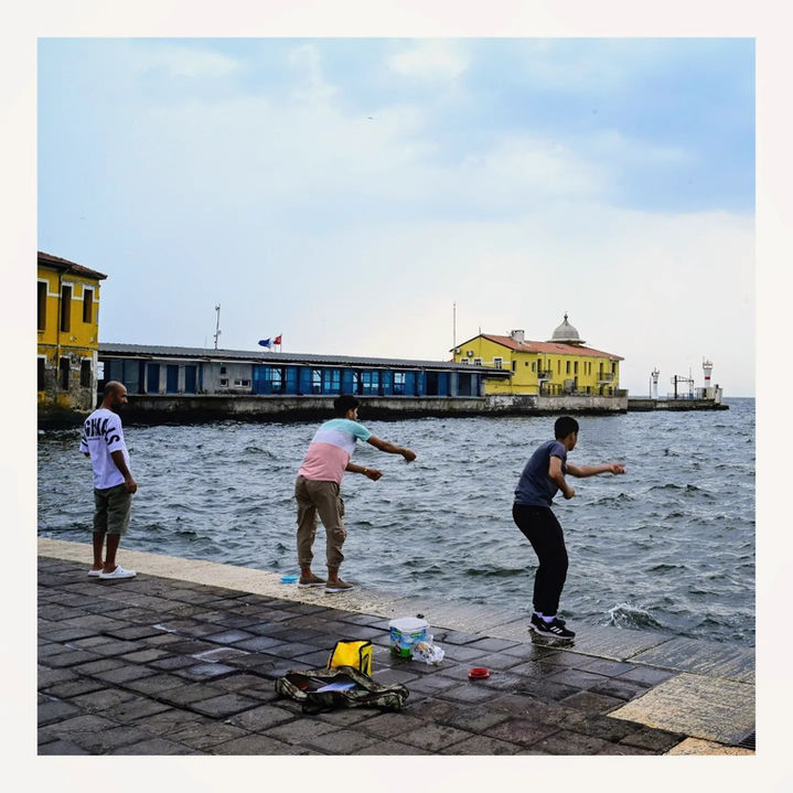 Three men fishing from a stone quay by the sea.