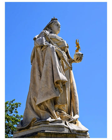 Weathered stone statue of Queen Victoria against a clear blue sky.