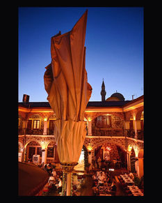 Fabric sculpture in front of illuminated historical courtyard with minaret at twilight.