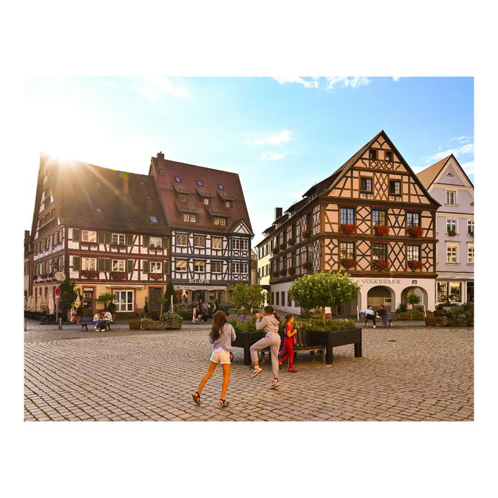 Sunny European town square with traditional half-timbered buildings and people.