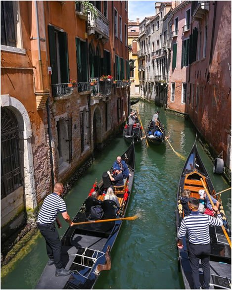 Gondolas with passengers navigating narrow canal bordered by historic Venice buildings.
