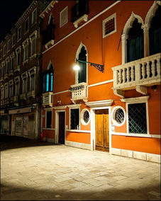 Vibrant orange Venetian building with ornate balcony illuminated at night.