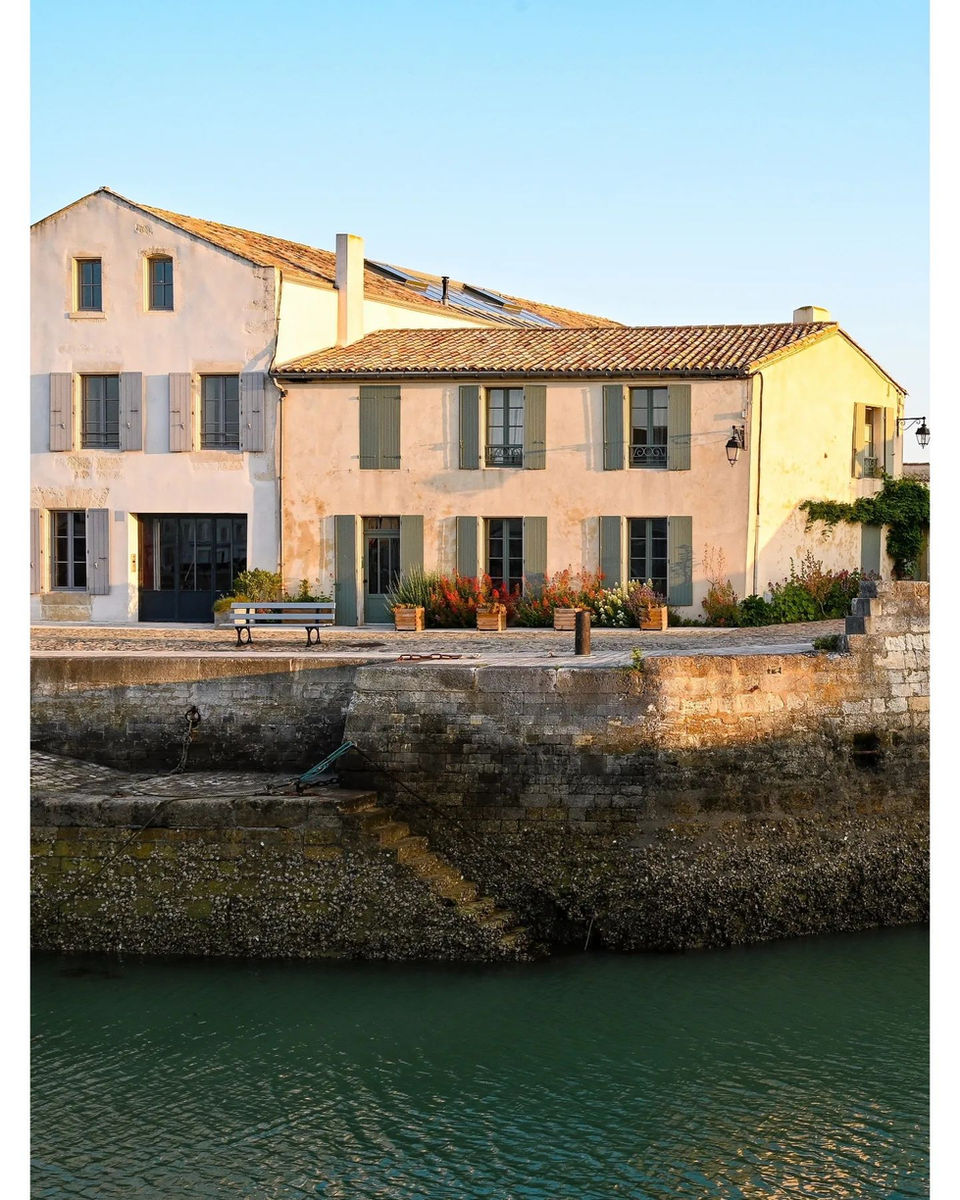 Charming European buildings with shutters lining a green canal under blue sky.