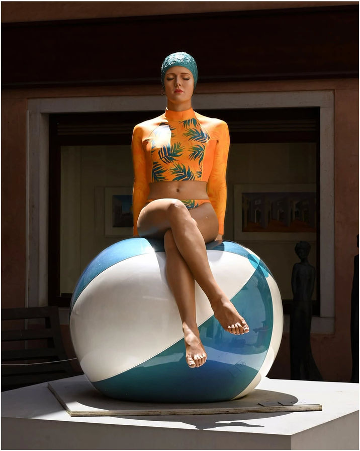 Sculpture of a woman in orange swimsuit sitting on a blue beach ball.