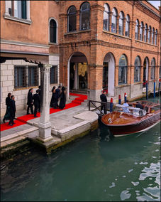 People walking red carpet to wooden boat on canal in Venice.
