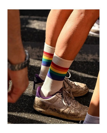 Person's legs wearing white socks with rainbow stripes and brown shoes outdoors.