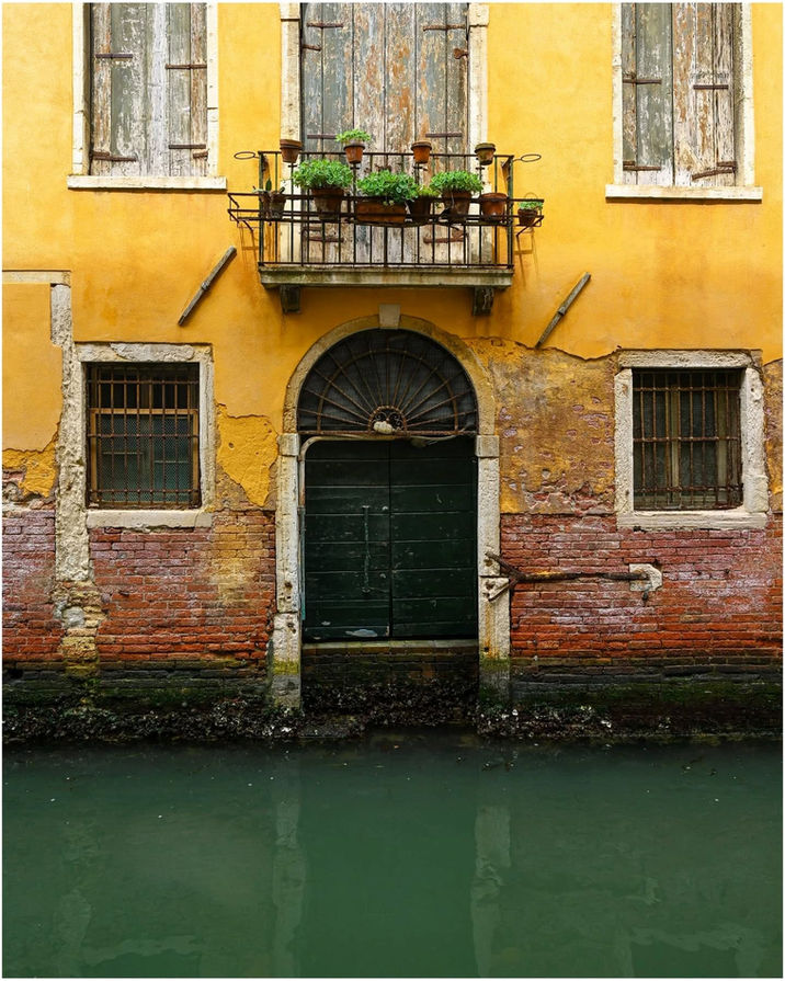 Old yellow Venetian building with dark door directly on green canal.