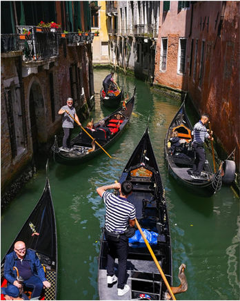 Gondolas with gondoliers and passengers navigate a narrow canal in Venice.