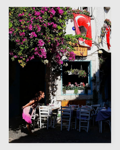 Woman in pink admires vibrant bougainvillea, Turkish flags on a charming cafe street.