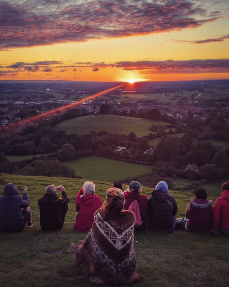 Group watches sunset, a bright light beam across the rural landscape.