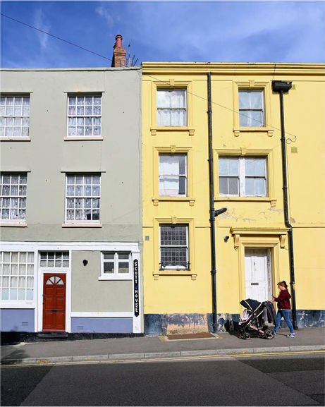 Colorful grey and yellow terraced houses with a person and pram.