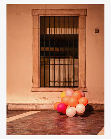 Colorful balloons piled on the ground below a barred window.