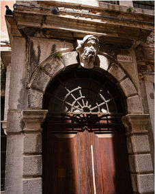 Ornate arched stone doorway with carved head, decorative ironwork, and wooden door.