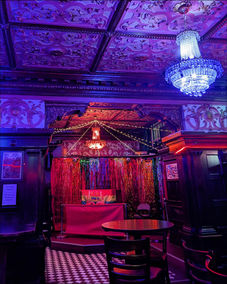 Colorful bar interior, ornate ceiling, chandelier, and small stage with streamers.