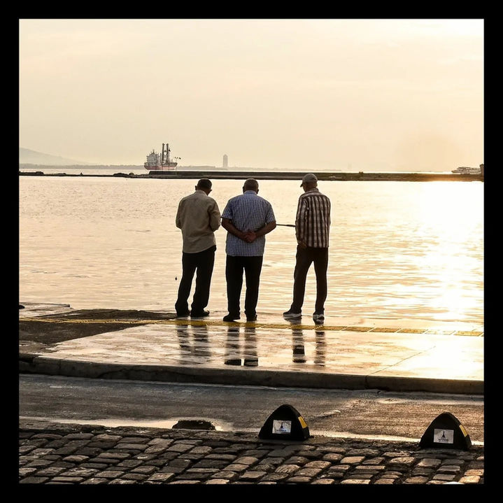 Three men standing by golden water, looking at distant city skyline.
