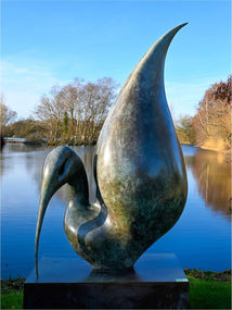 Abstract bronze bird sculpture with a large wing by a reflective lake.