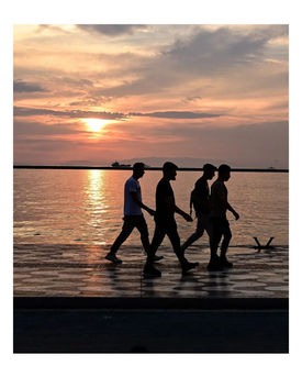 Four people walking in silhouette against a beautiful sunset over water.