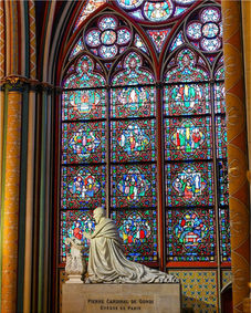 Kneeling statue before large, intricate stained glass window in a cathedral.