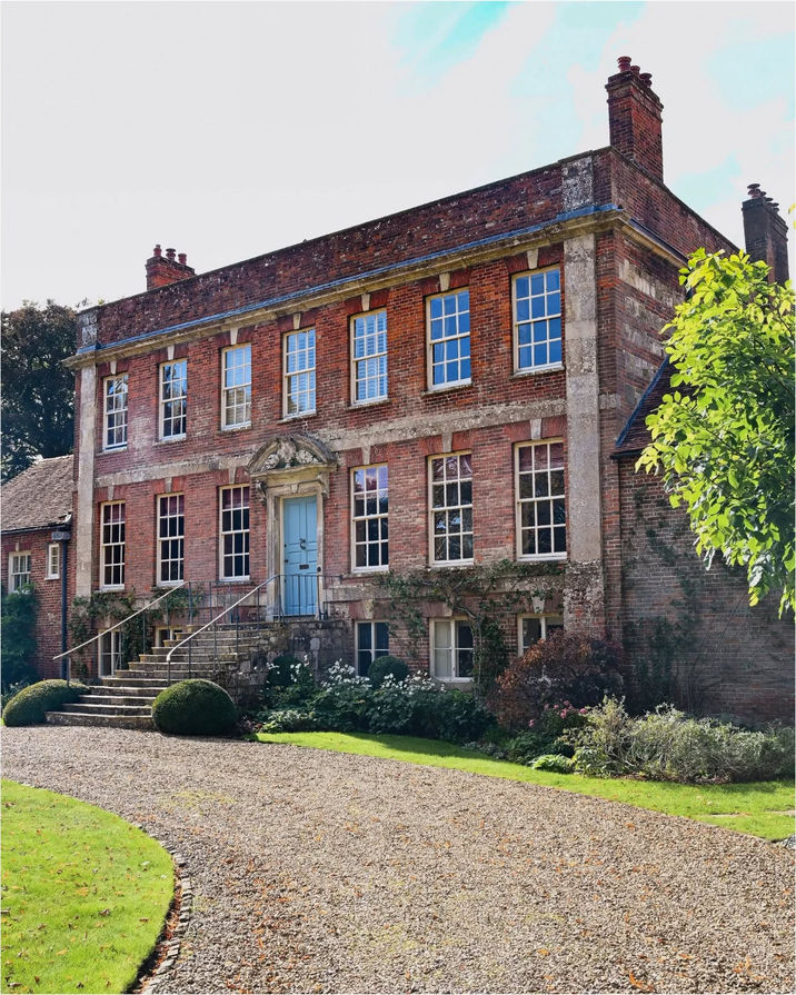 Elegant red brick manor house with blue door and gravel driveway.