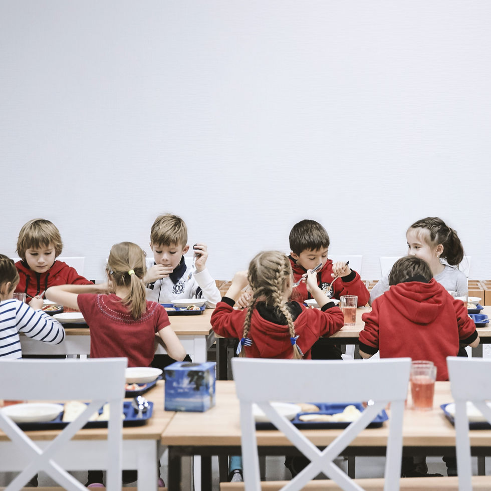 Children sitting together in a school cafeteria, eating lunch and chatting at a long table.
