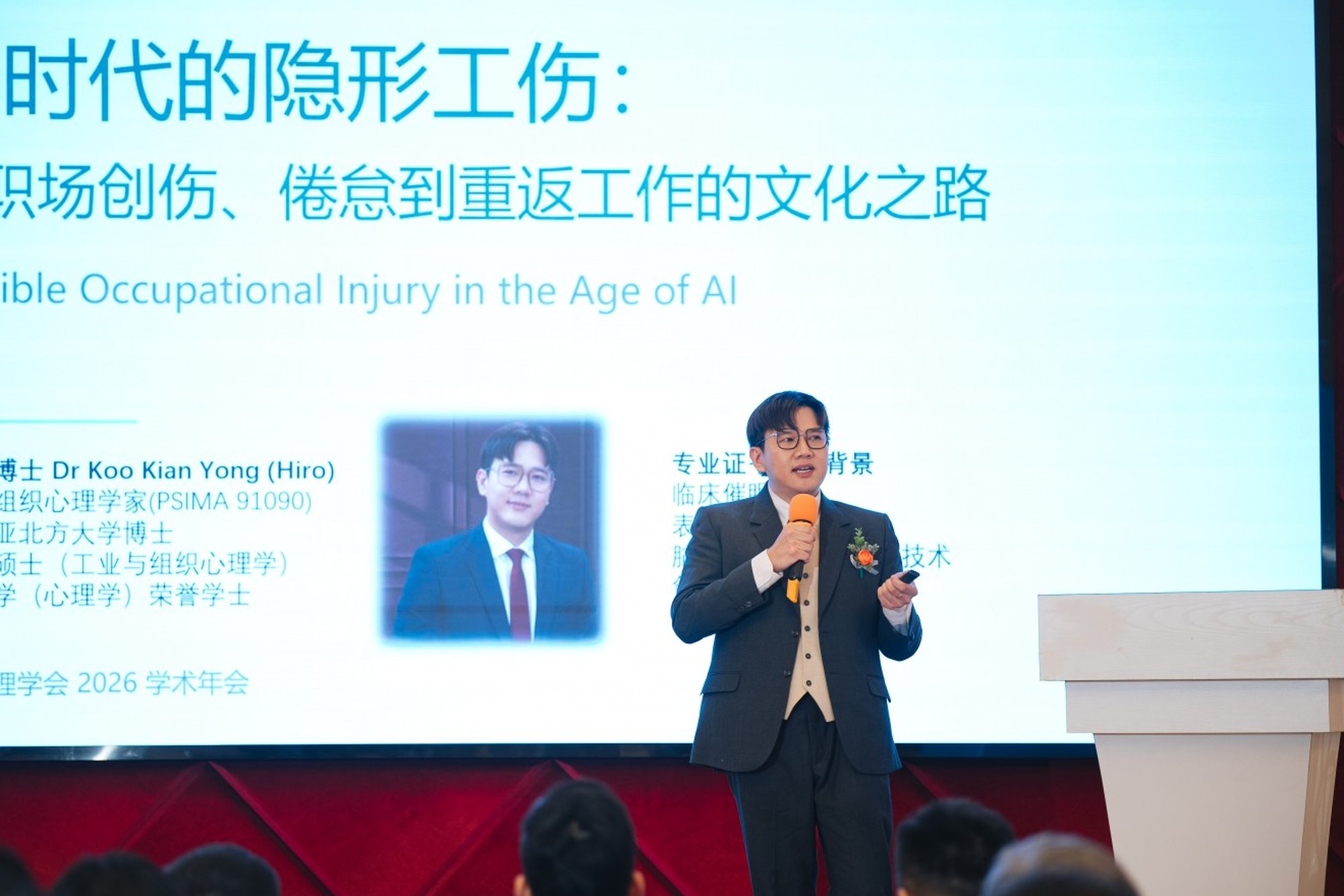 Dr Koo Kian Yong (Hiro) at the podium; slide reads Invisible Occupational Injury in the Age of AI.