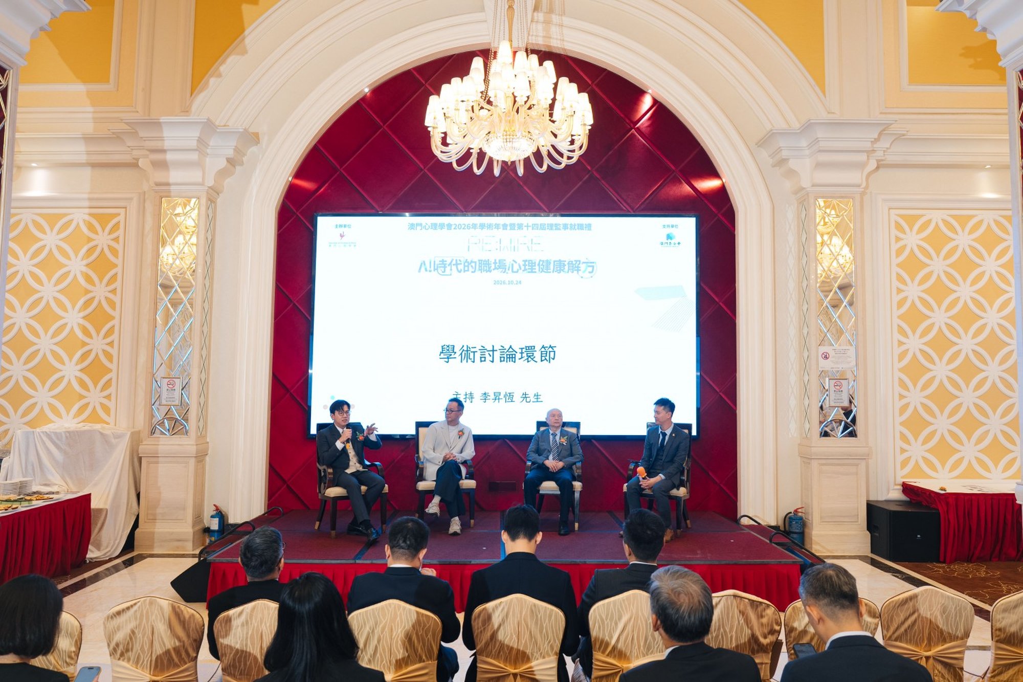 Four speakers on stage; screen shows Macau Psychology Association 2026 annual conference title.