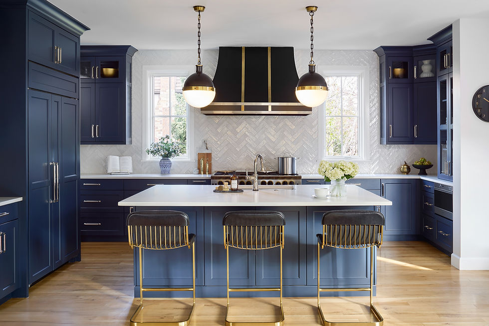 Stunning kitchen with navy blue cabinets, white herringbone tile backsplash, hidden appliances, gold and black barstools, hood and pendant lights.