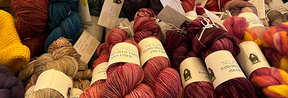 An array of hand dyed yarns in colors of purples, pinks and tan as well as hand spun yarn in blue and pink.
