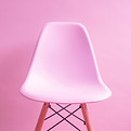 A pink stacking plastic chair on a pink background