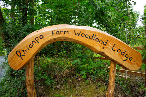 Handcrafted Rhianfa Farm Woodland Lodge sign welcoming guests to holiday accommodation in West Wales.