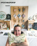 A maker smiling in front of her homemade market stall displaying animal themed products.