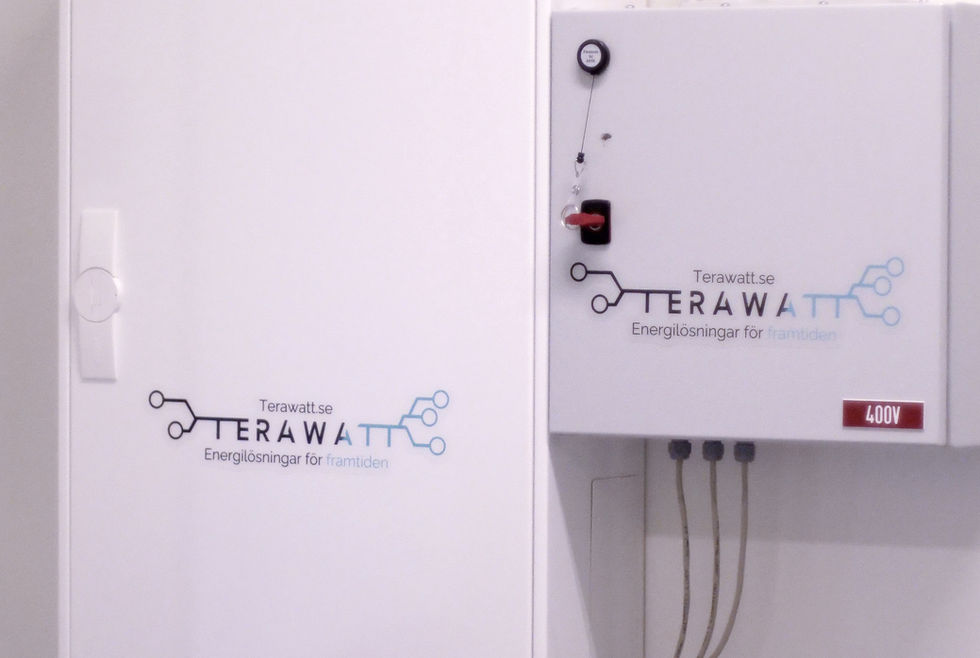 Ett stort vitt fördelningskåp märkt TERAWATT med inkommande kablar, en logotyp och text på framsidan. Det är placerat mot en vit vägg bredvid ett litet elektriskt kontrollskåp.