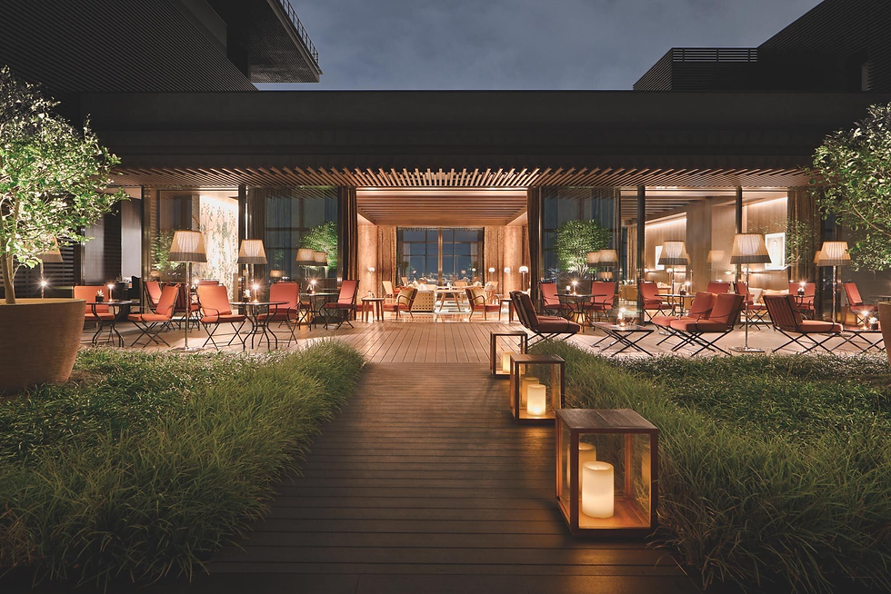 Outdoor lounge with red chairs and tables, surrounded by greenery and lit lanterns. Warm ambiance under a modern wooden pergola at night.