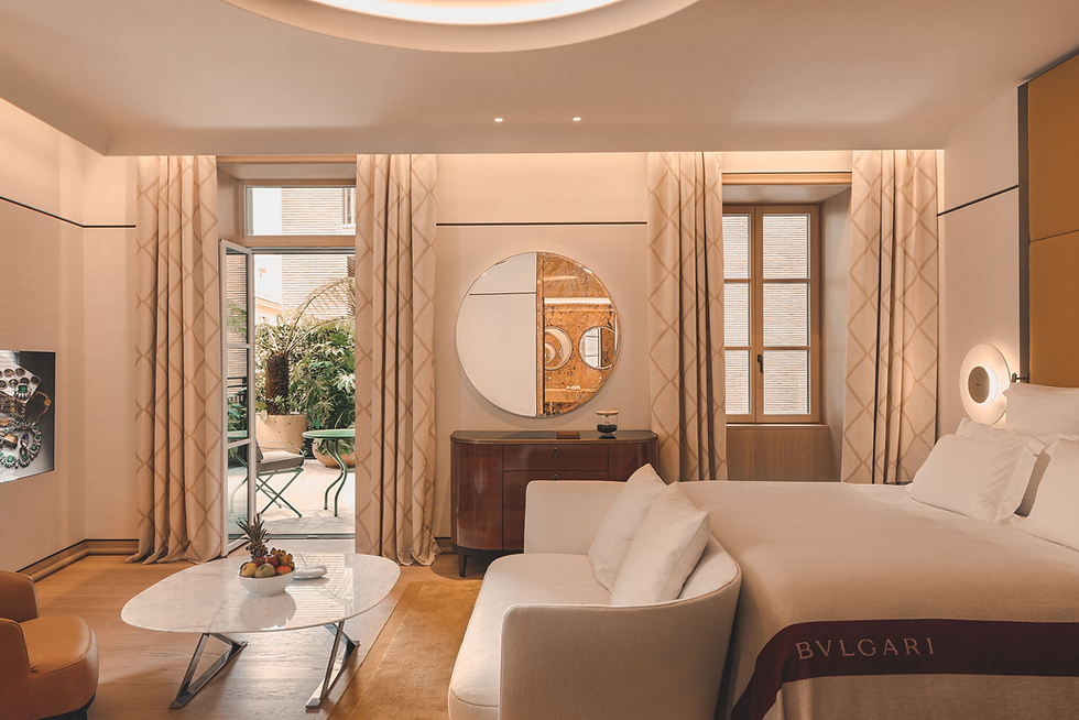 Luxurious hotel room with a plush bed, a mirror, and balcony doors leading to greenery. Soft lighting, neutral tones, and a table with fruit.