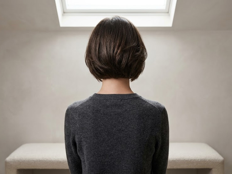 An autistic person stands alone in a dim room, lit from above, shoulders slightly tense, symbolizing the hidden weight of masking in everyday life.