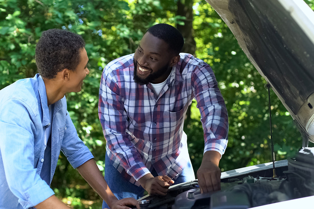 Dad and teen son looking under the hood of car